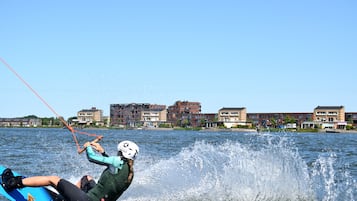 Une personne fait du wakeboard sur un lac, avec des bâtiments en arrière-plan.