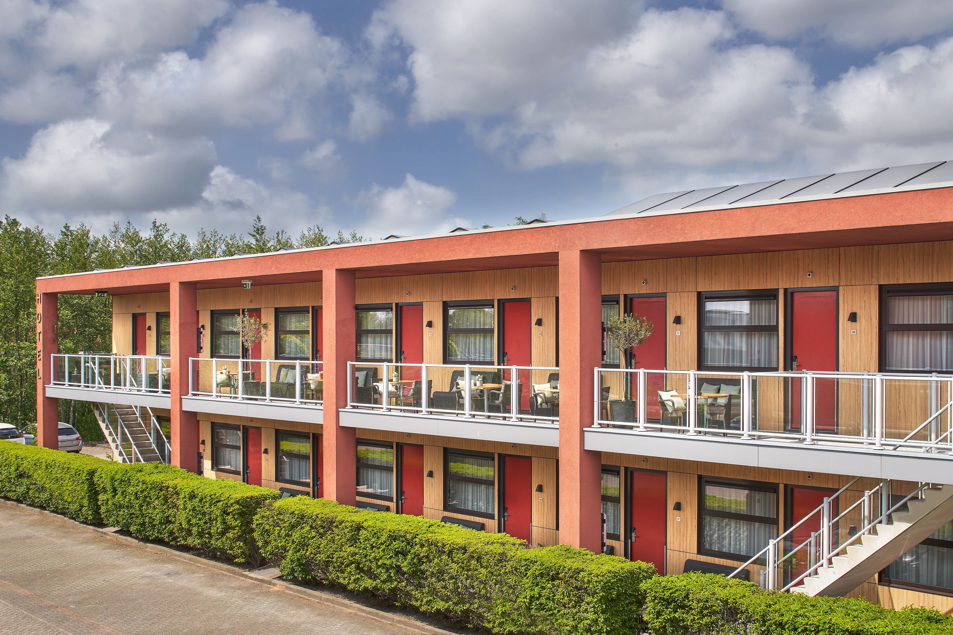 Un hotel moderno con fachada roja, varios balcones y una escalera que lleva al piso superior.