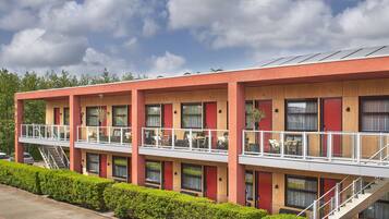Un hotel moderno con fachada roja, varios balcones y una escalera que lleva al piso superior.