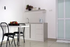 A modern kitchen with a white countertop, two black chairs, a white kettle, and a potted plant on the shelf.