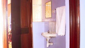 A bathroom with a sink, a towel hanging on the wall, and a wooden door. - Gemco Lodge (Embu)