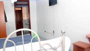 A hospital bed in a room with a wooden door, a wall-mounted TV, and a blue mat on the floor. - Gemco Lodge (Embu)
