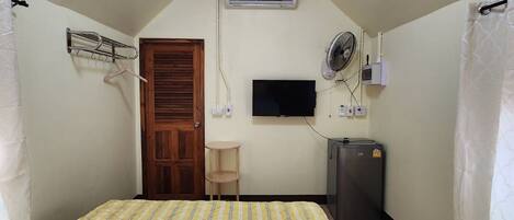 Una habitación pequeña y luminosa con cama, televisión, aire acondicionado y ventilador.