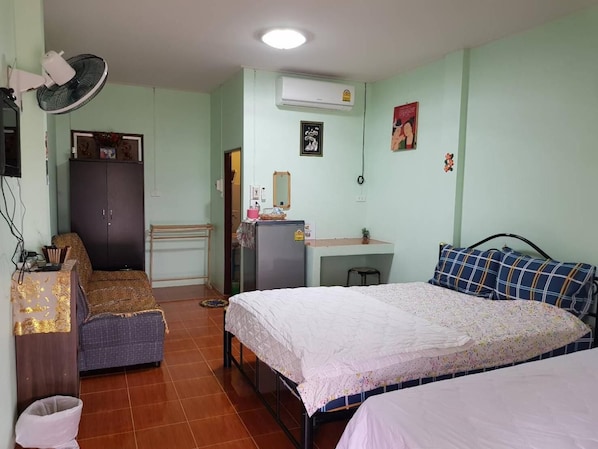 A dormitory room with two beds, a desk, a wardrobe, and an air conditioning unit.