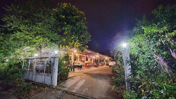 A pathway leading to a building with outdoor seating, surrounded by greenery and illuminated by street lamps.