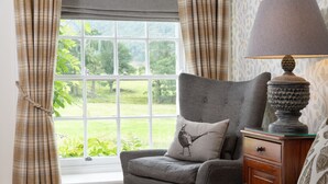 A bedroom with a window, a chair with a pillow, a lamp, and a bedside table.