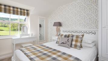 A bedroom with a large bed, a dresser, a mirror, and a window with a view of a green landscape.