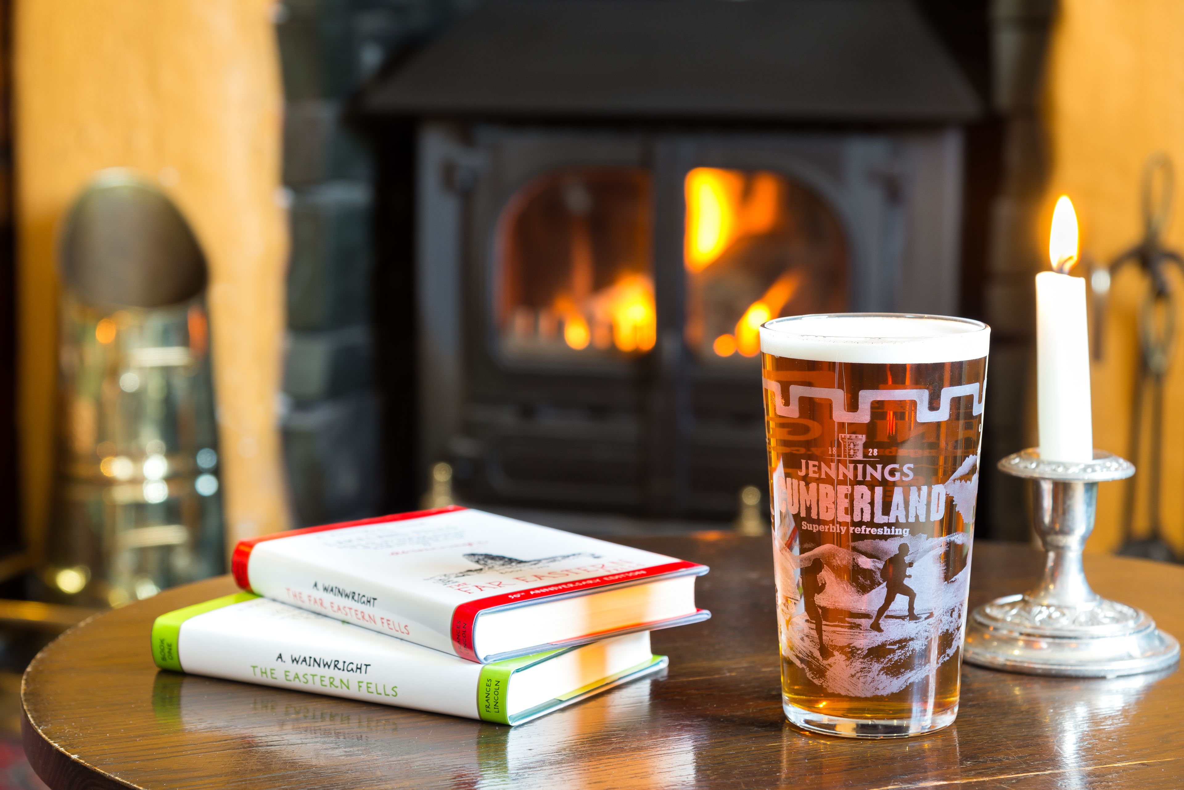 A table with a glass of beer, a candle, and books.
