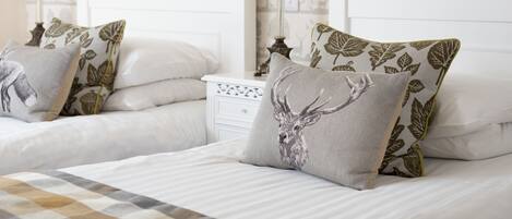 A bedroom with two beds, each with a pillow featuring a deer design. There are two bedside lamps and a white nightstand between the beds.