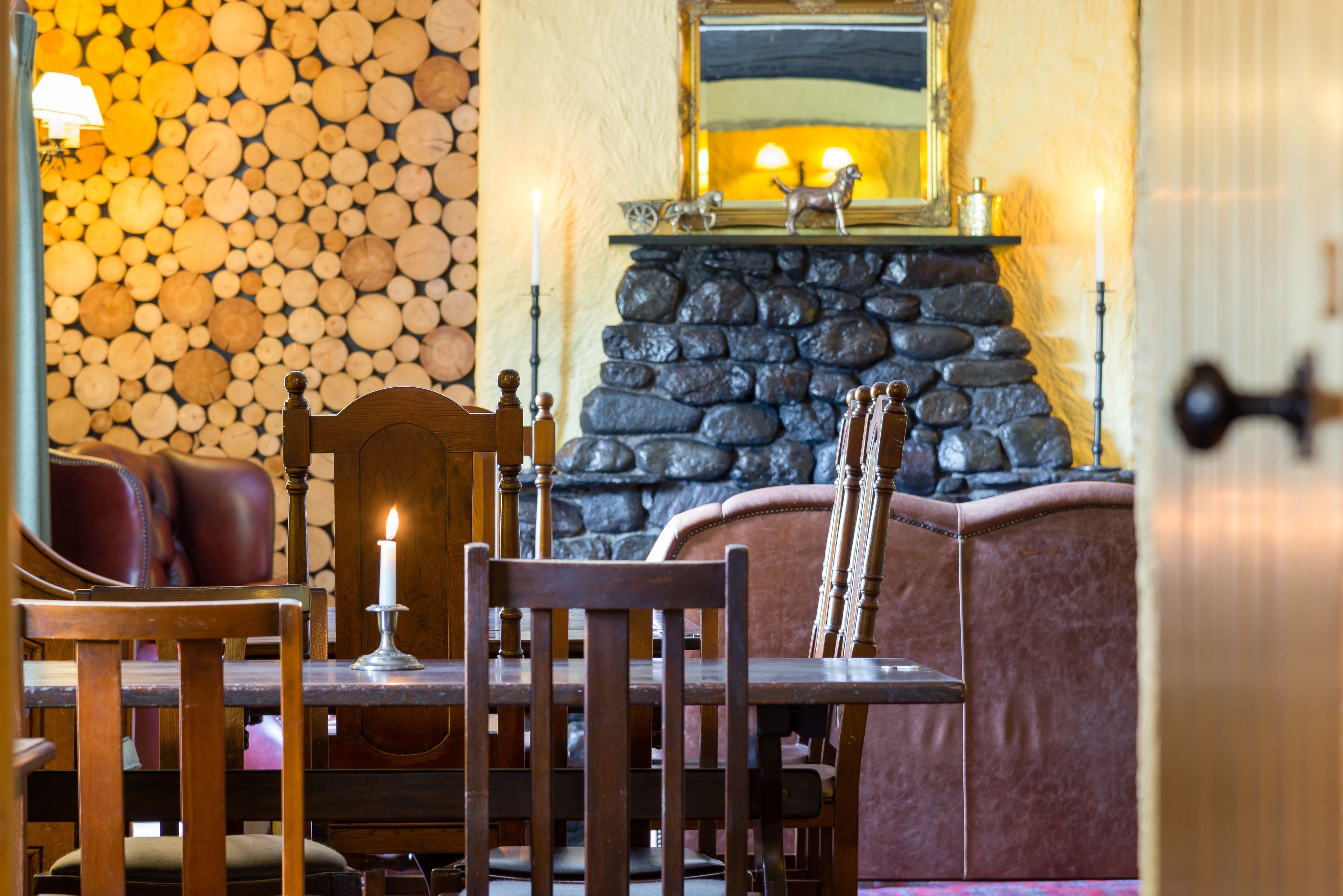 A cozy dining area with a stone fireplace, wooden furniture, and a candle on the table.