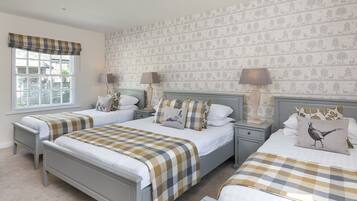 A bedroom with two beds, a window with a checkered valance, patterned wallpaper, and bedside lamps.