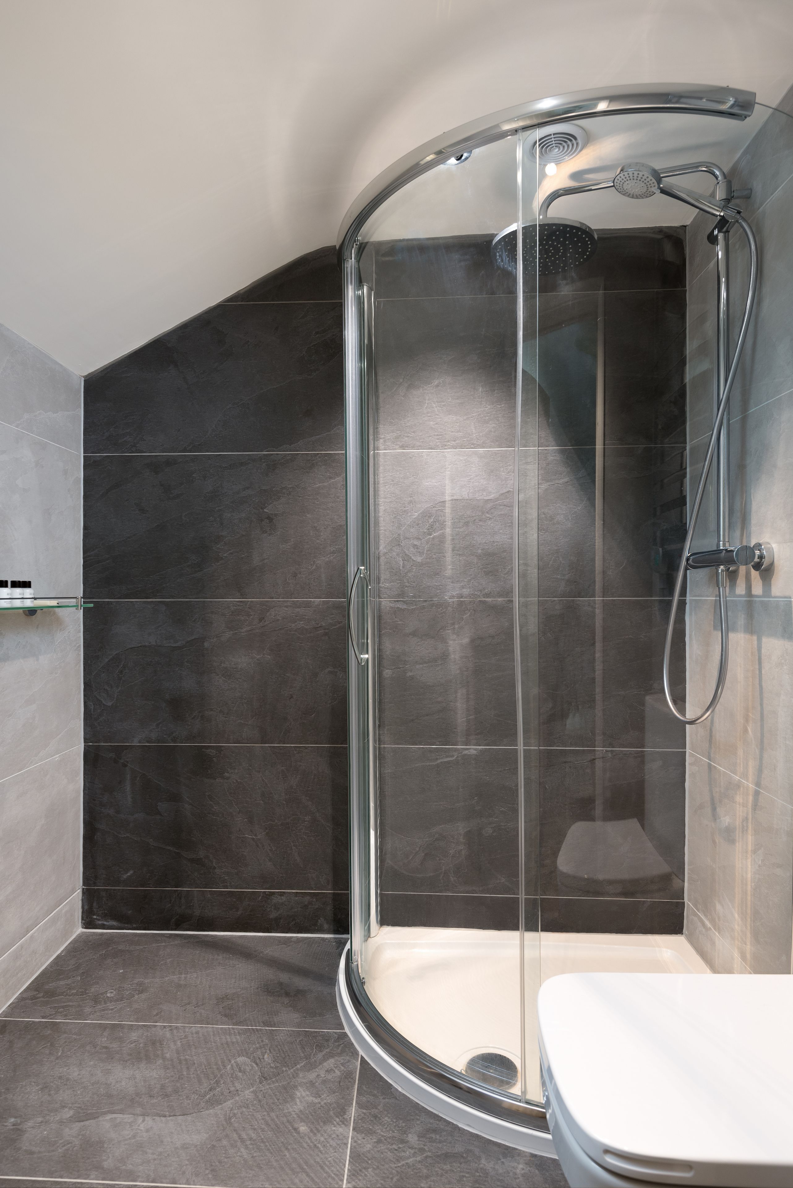 A modern bathroom with a glass-enclosed shower, dark tiles, and a white toilet.