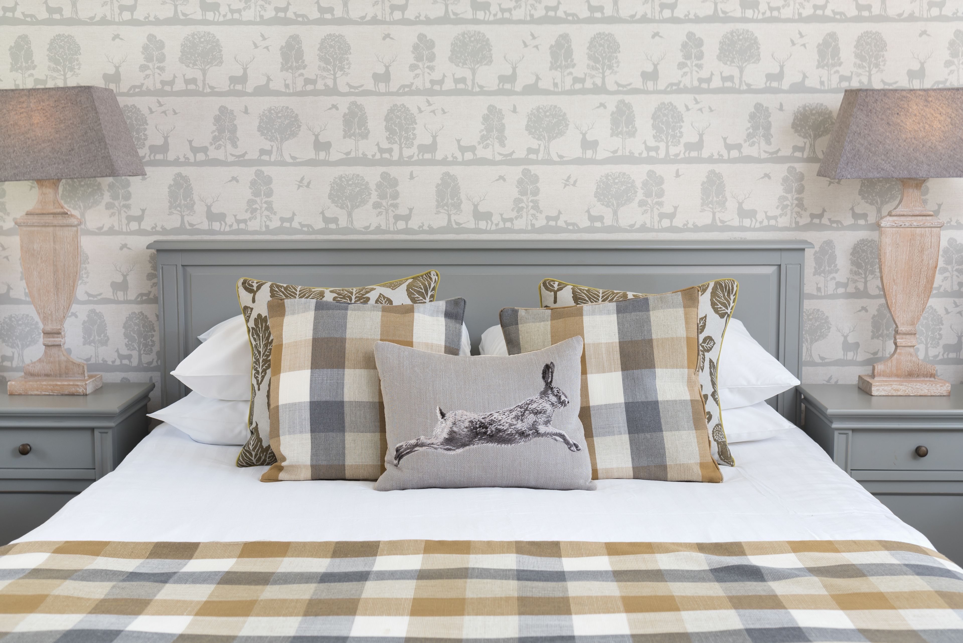 A neatly made bed with a checkered bedspread, flanked by two nightstands with lamps and a patterned wallpaper background.