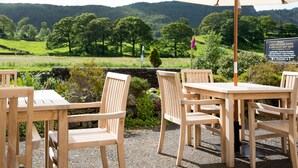 Outdoor wooden tables and chairs with a view of a green landscape and hills in the background.