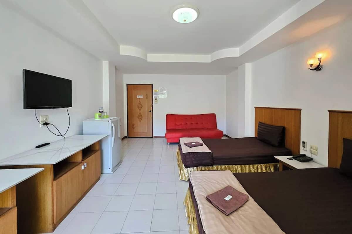 A hotel room with a bed, a desk, a television mounted on the wall, a red sofa, and a door.