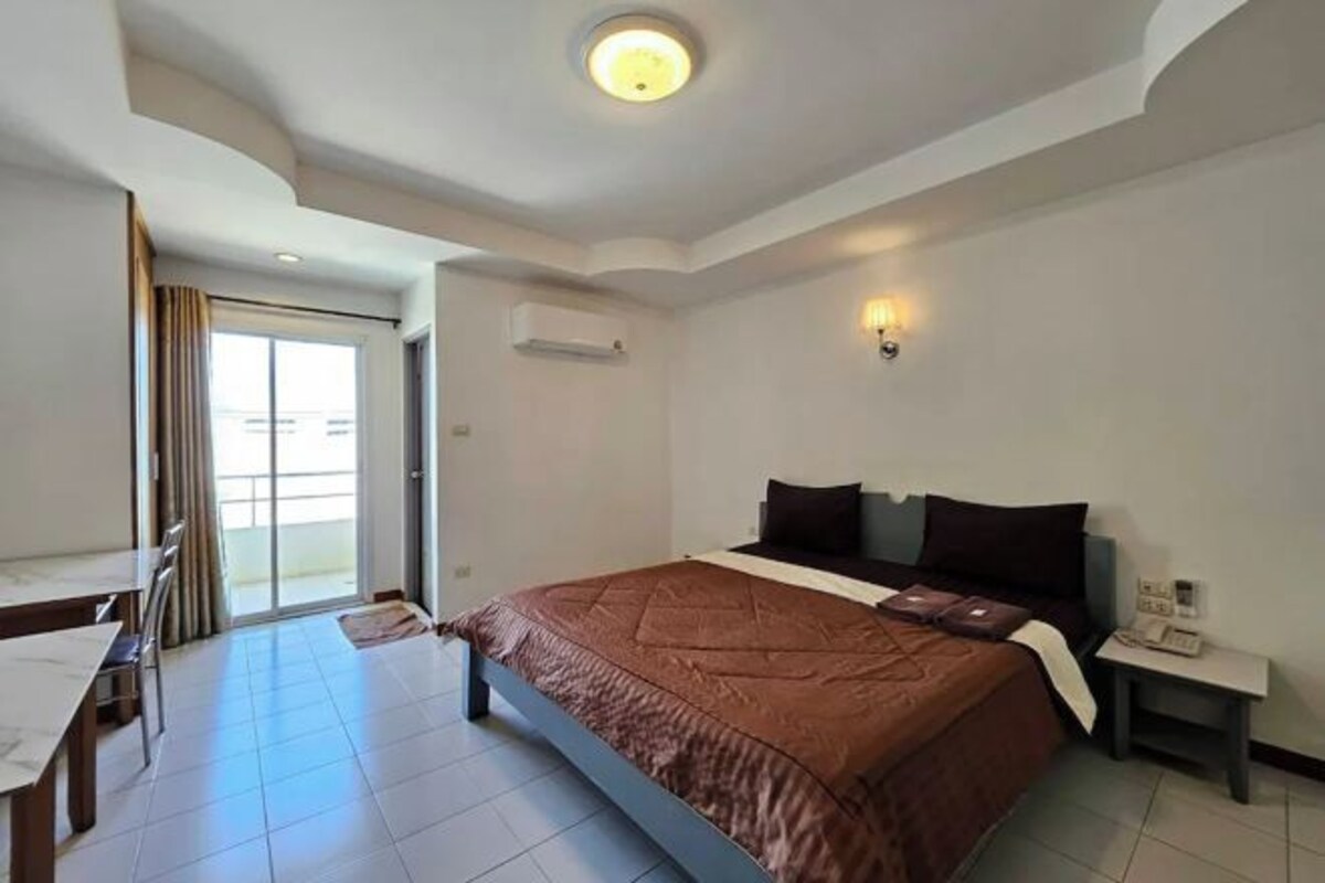 A hotel room with a bed, a desk, a chair, a small table, a nightstand, and a wall-mounted phone.