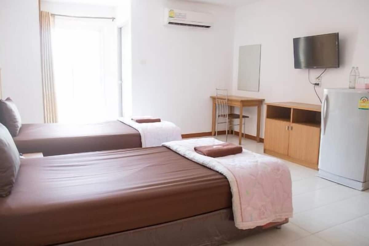 A room with two beds, a desk, a chair, a television, and a refrigerator.