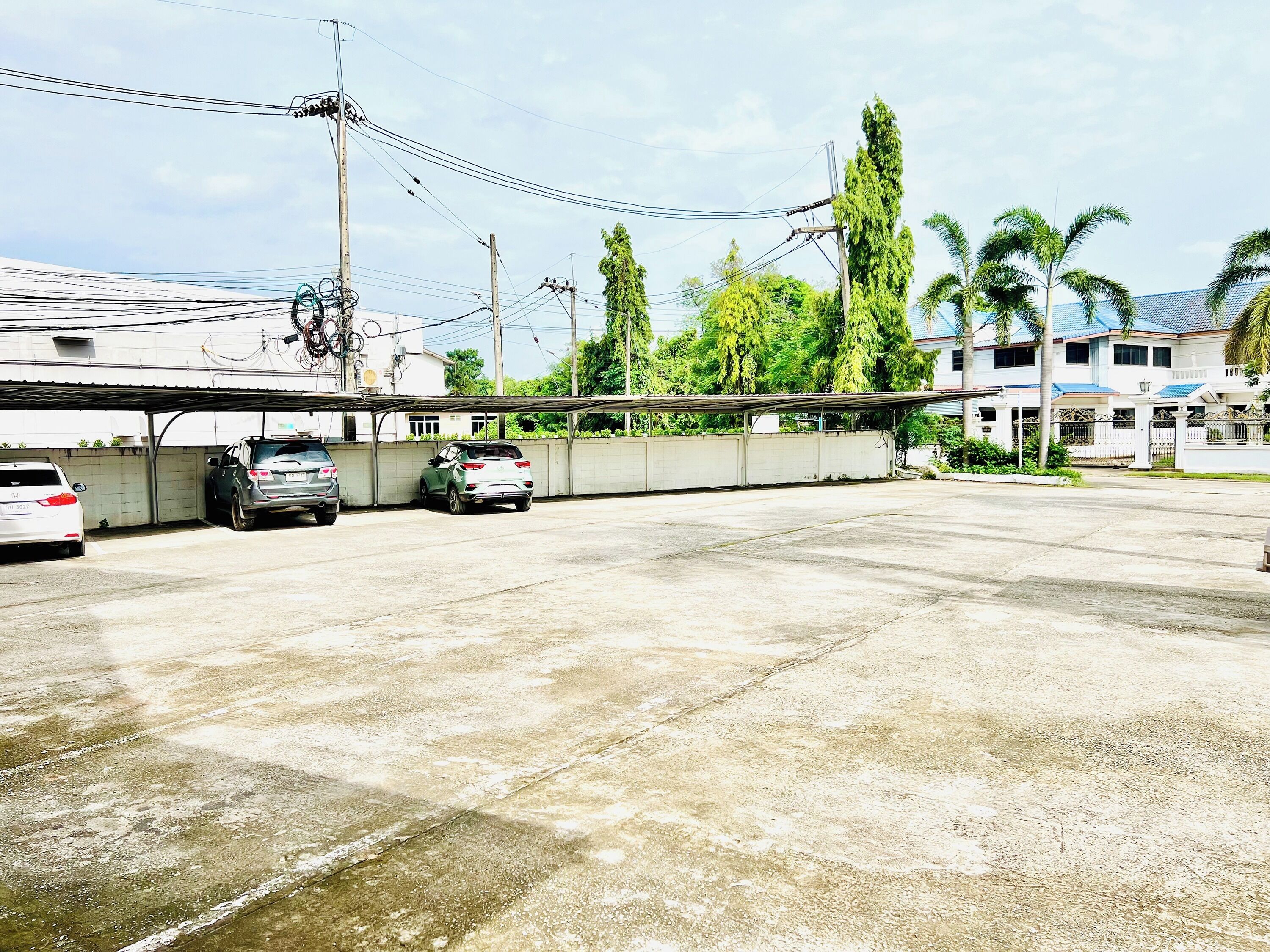 A parking area with two cars, a covered structure, and a building with a blue roof.
