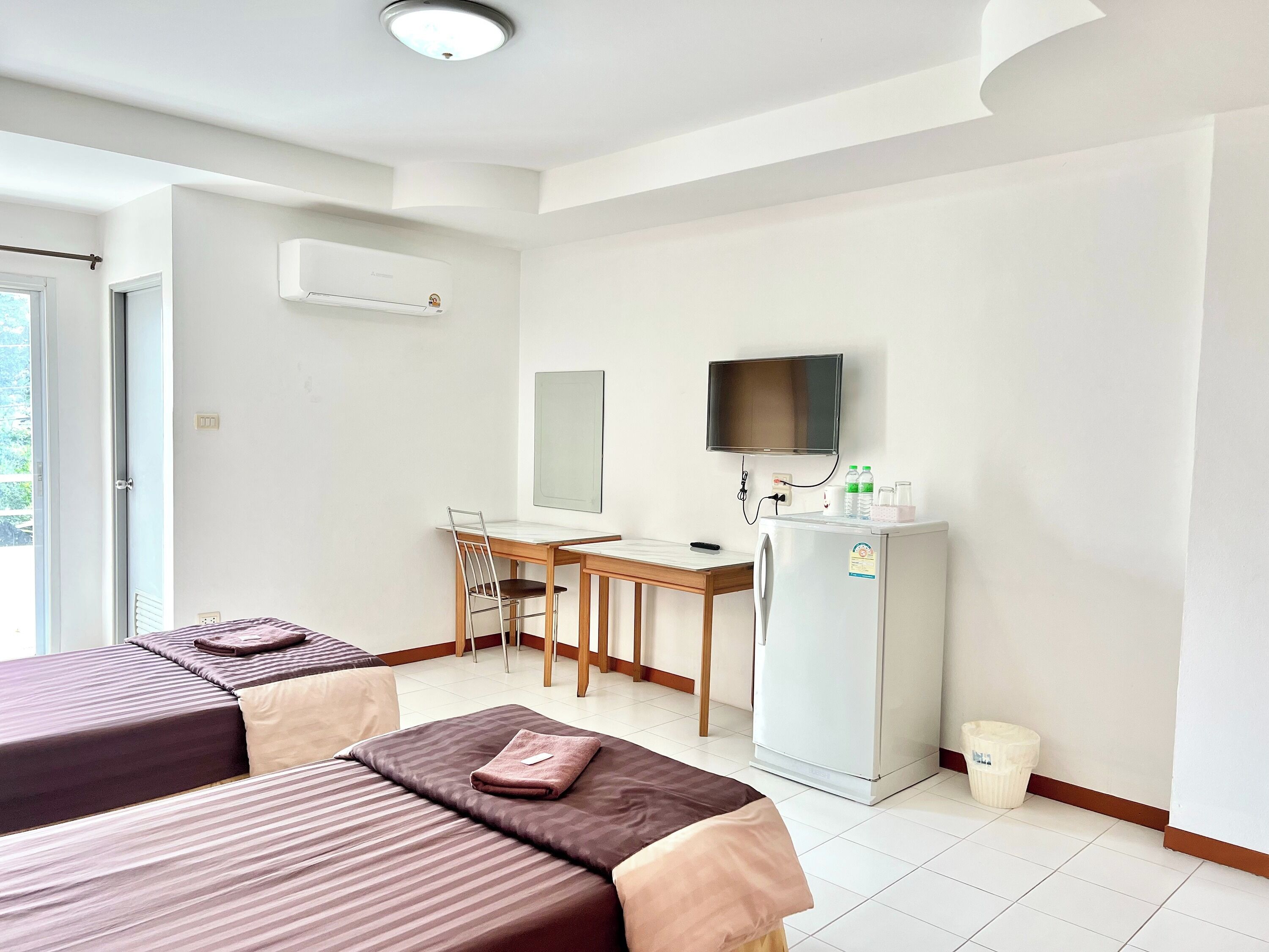 A hotel room with two beds, a desk with a chair, a television, and a refrigerator.