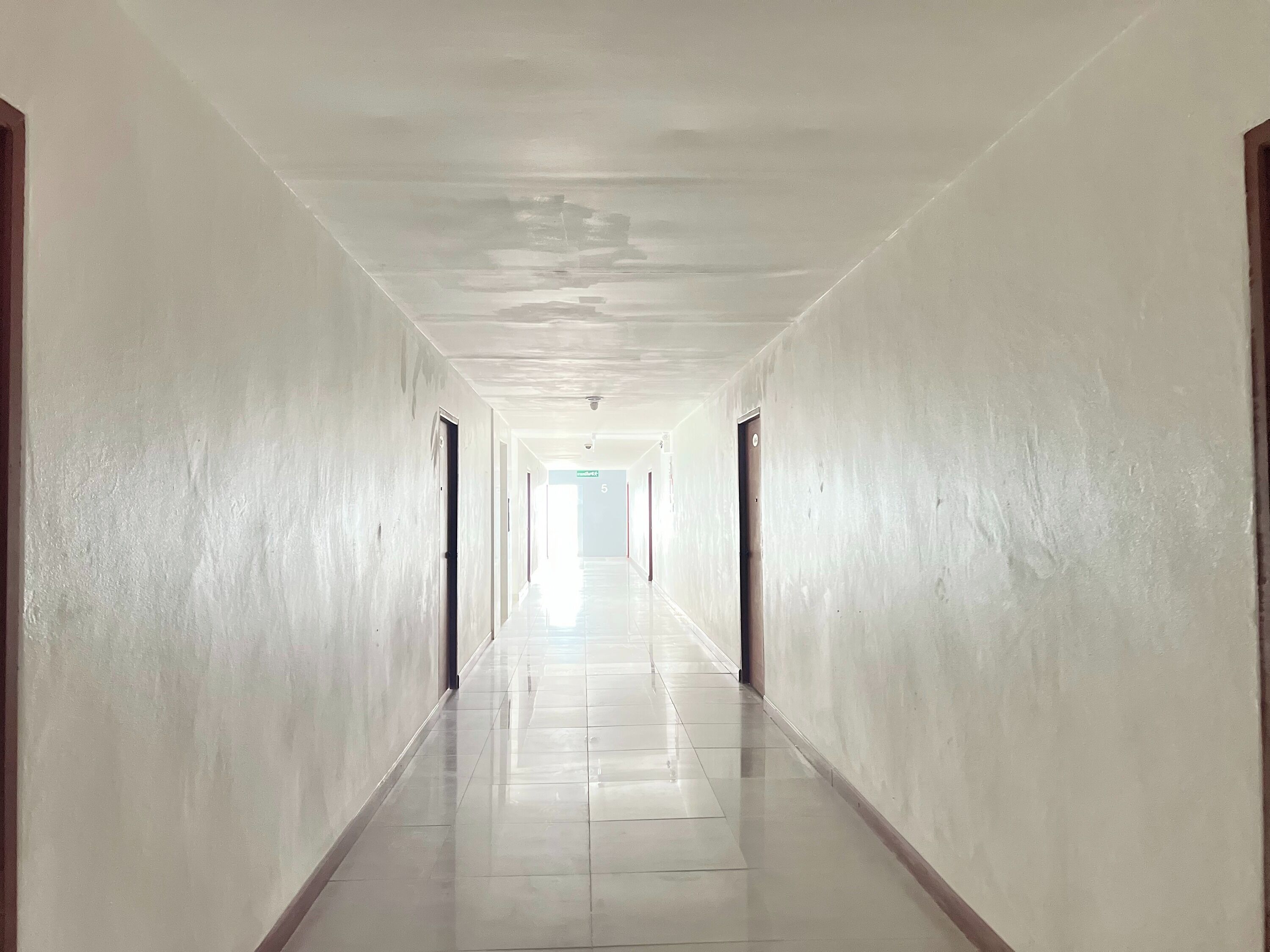 Un long couloir étroit aux murs blancs et au sol carrelé brillant.