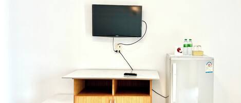 A room with a television mounted on the wall, a wooden cabinet with two doors, a small table, and a refrigerator.