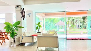 A spacious living area with a large glass door leading to an outdoor garden. There are two white sofas and a wooden chair. A potted plant is visible on the left side. - BT Grand Condotel (Udon Thani)