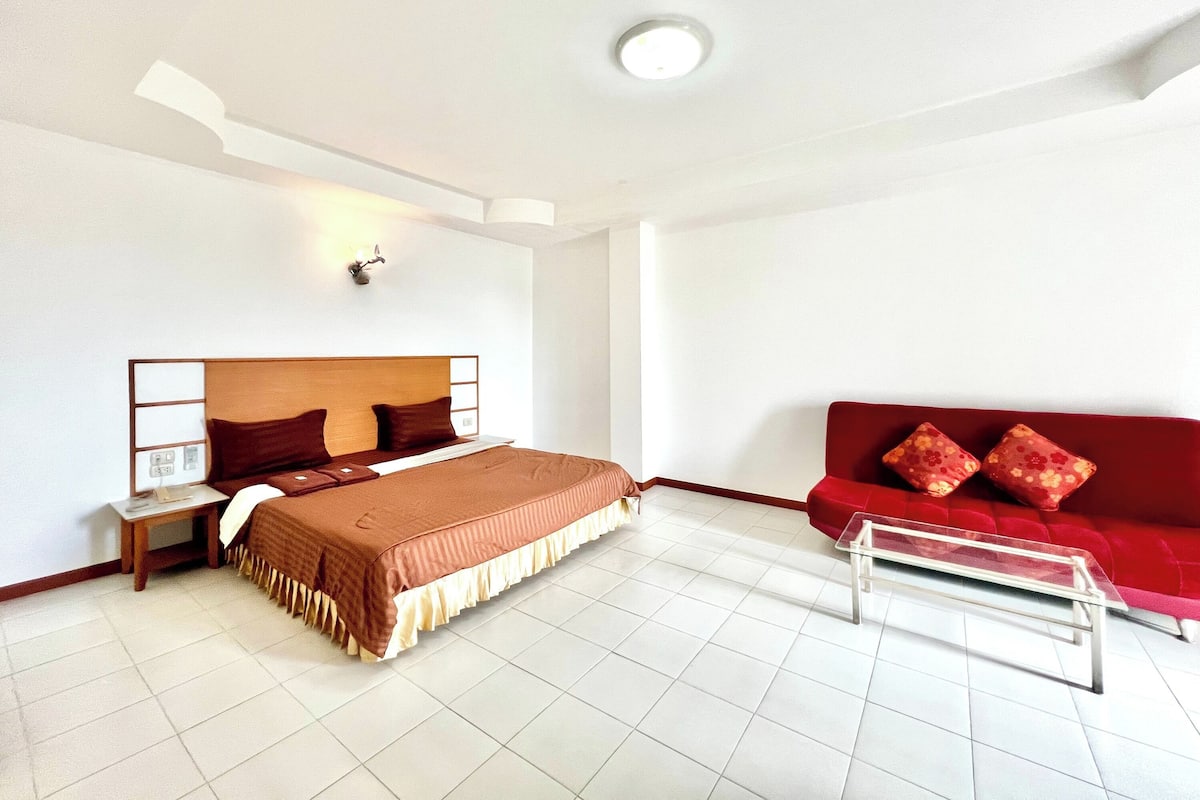 A hotel room with a bed, a red sofa, a small table, and a nightstand.