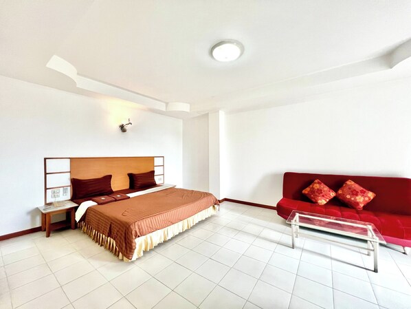 A hotel room with a bed, bedside table, lamp, red sofa, and a glass coffee table. - BT Grand Condotel (Udon Thani)