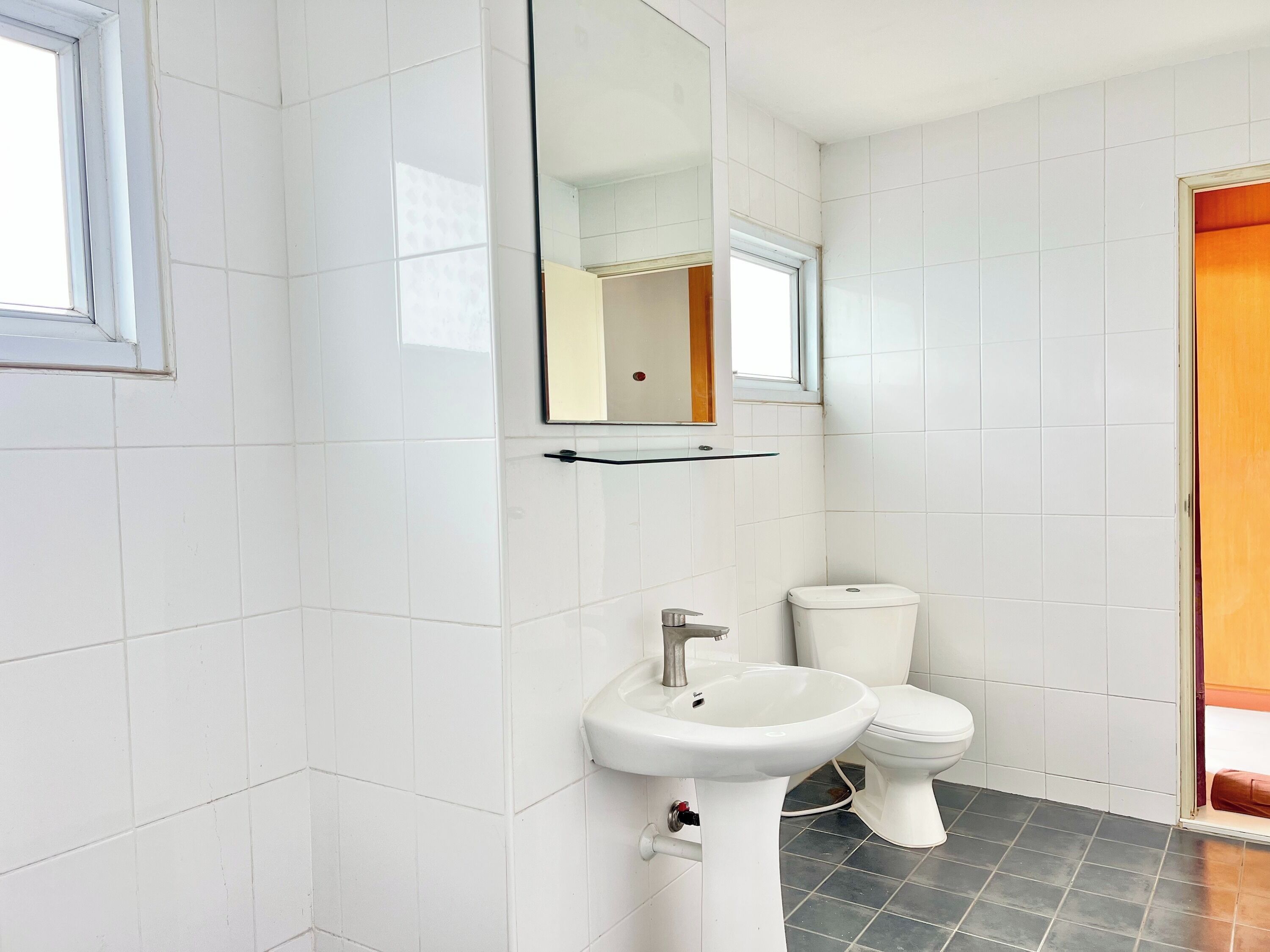 Une salle de bain avec des carreaux blancs, un lavabo blanc, des toilettes et un miroir.