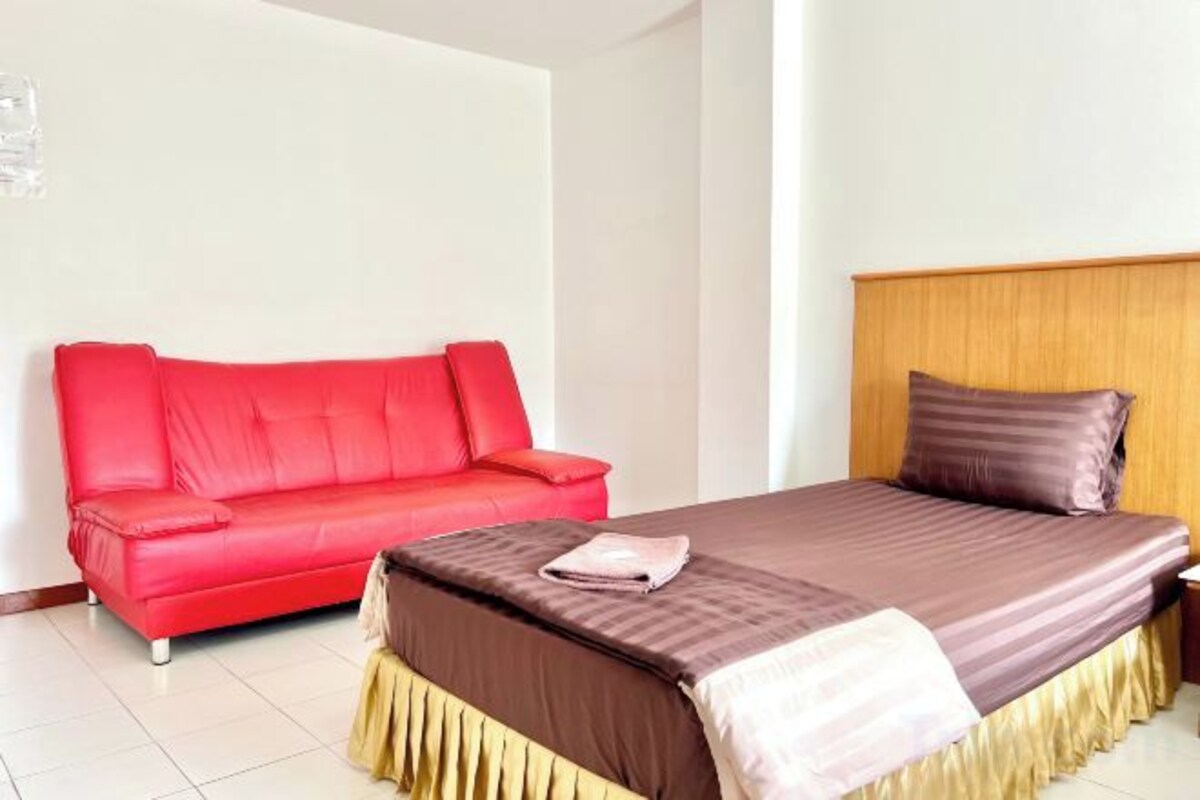 Una habitación de hotel con una cama, un sofá rojo y un cabecero de madera.