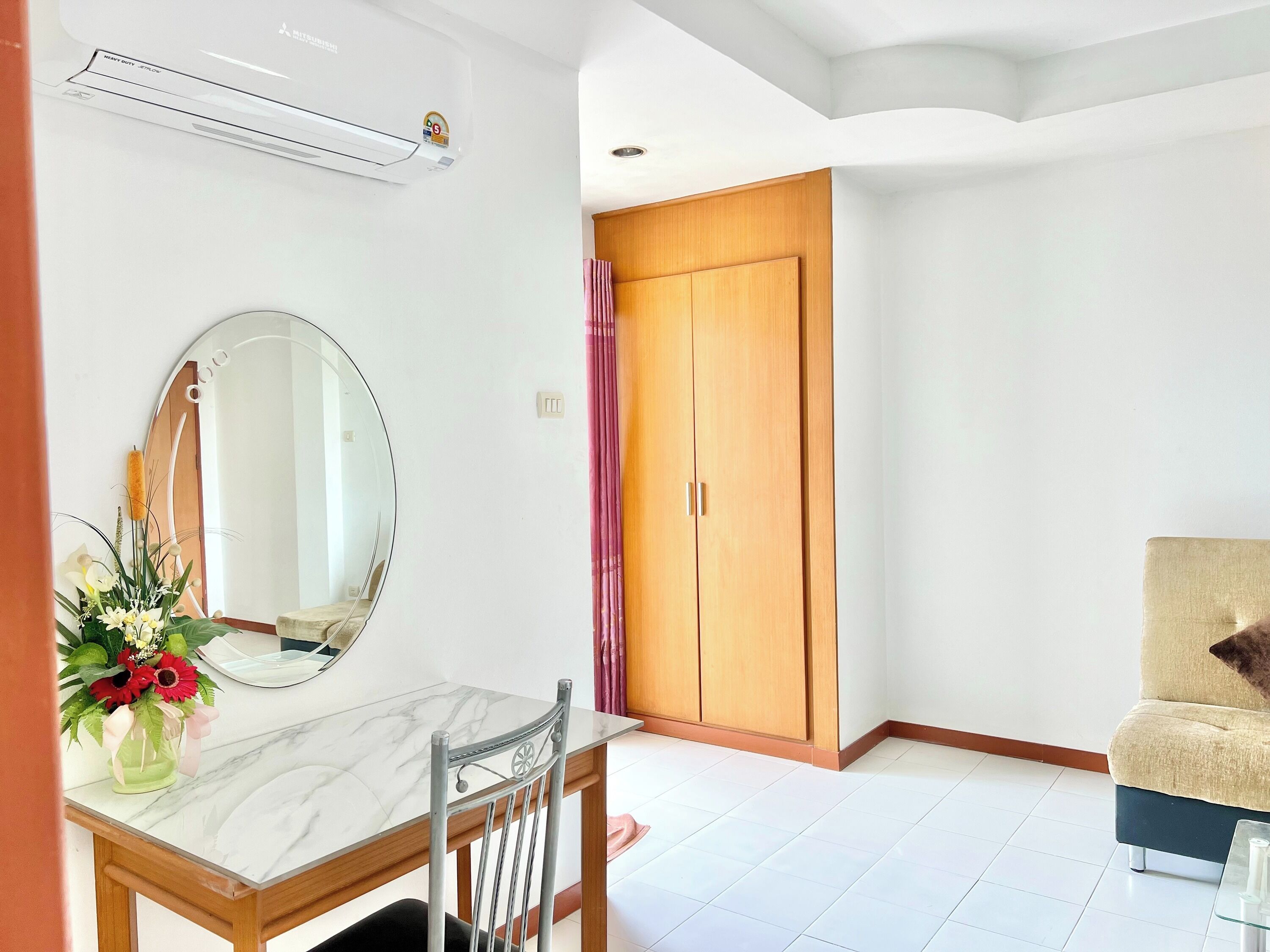 A room with a dining table, a chair, a mirror, a wooden wardrobe, and a sofa.