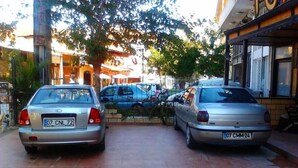 Two parked cars on a tiled street with buildings and trees in the background. - Sunrise Hotel (Antalya)
