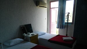 A room with two beds, a small desk with a mirror, a window with curtains, and an air conditioning unit. - Sunrise Hotel (Antalya)