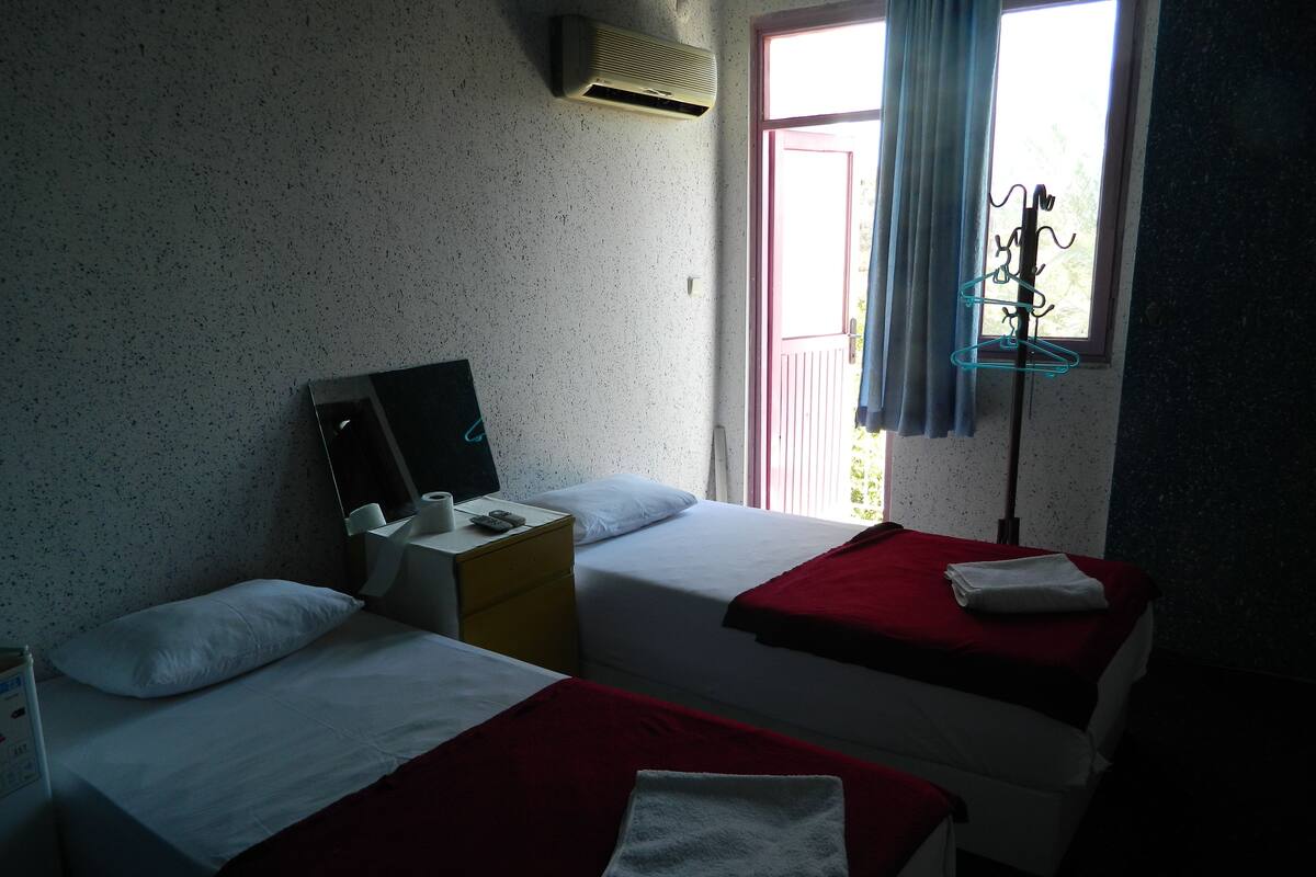 Una habitación con dos camas, un escritorio pequeño con espejo, una ventana con cortinas y un equipo de aire acondicionado.