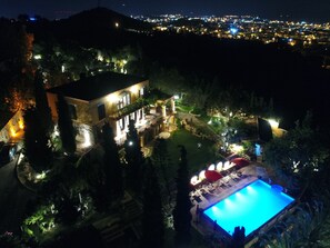 A large, illuminated swimming pool with a patio area, surrounded by trees and a well-lit building with multiple windows and balconies. - Villa Taraca Alacati Romantik Hotel (Cesme)