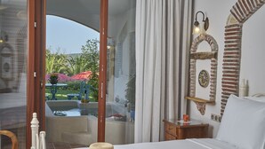 A bedroom with a bed, a nightstand, a decorative wall, and a view of an outdoor garden. - Villa Taraca Alacati Romantik Hotel (Cesme)