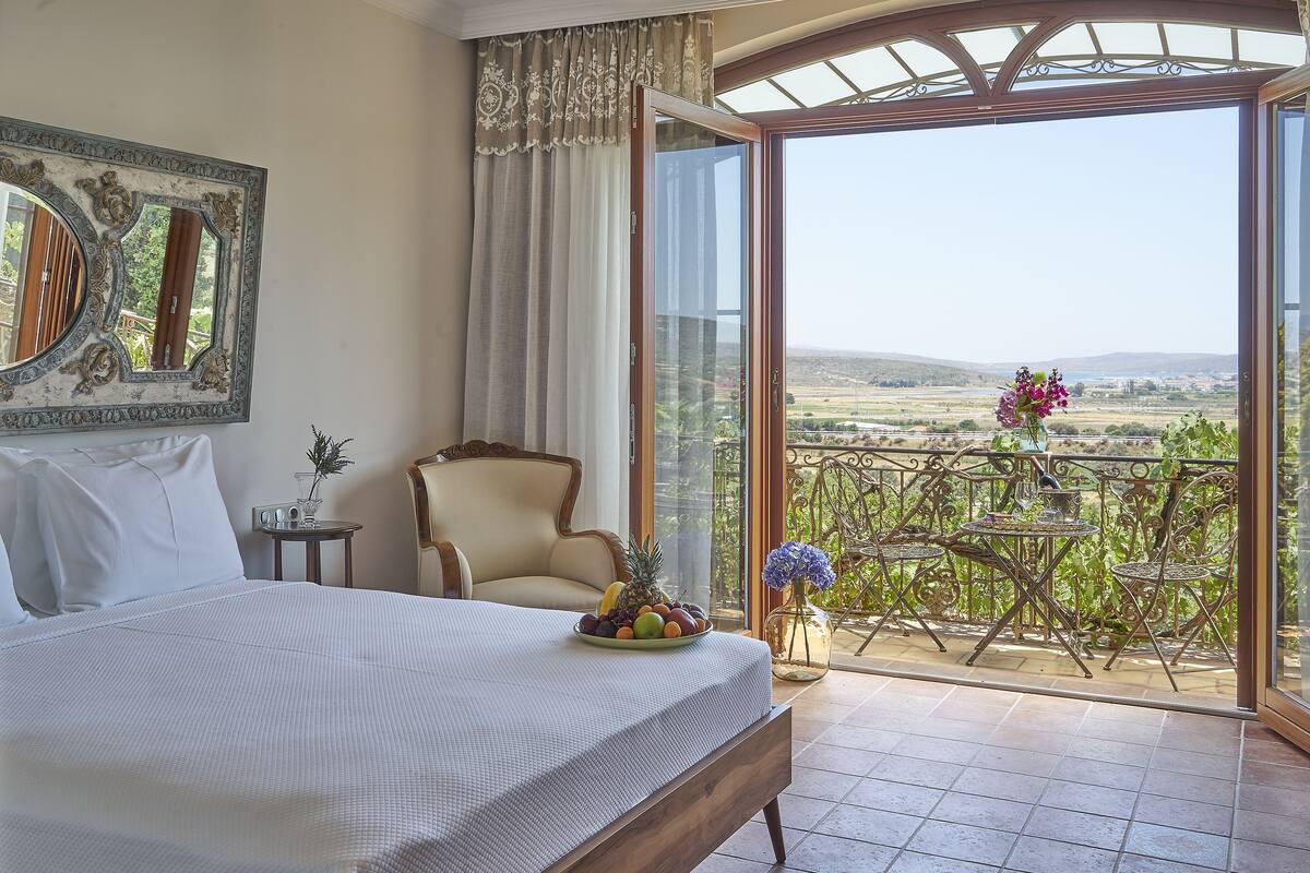 Een slaapkamer met een bed, een stoel, een tafel met fruit en een balkon met uitzicht.