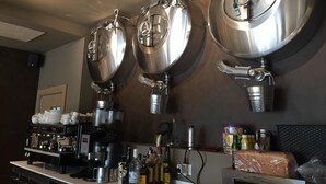 Una zona de bar con tres grifos de cerveza de acero inoxidable, una cafetera y diferentes botellas y vasos sobre la barra.
