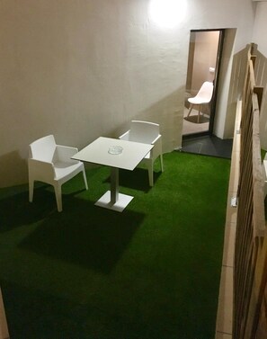 A room with a white table and four white chairs, a small white table lamp, and a green artificial grass floor. - Hotel Landaben (Pamplona)