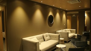 Un vestíbulo de hotel con un sofá color beige, sillones y un espejo redondo en la pared.
