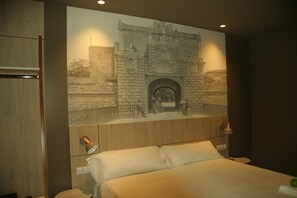 A hotel room with a bed, a wall-mounted TV displaying a historical scene, and a wooden headboard. - Hotel Landaben (Pamplona)