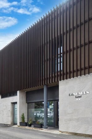 A modern hotel building with a vertical slatted facade, large glass entrance, and a visible name sign. - Hotel Landaben (Pamplona)