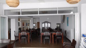 Un comedor con varias mesas y sillas, un espejo grande y lámparas de techo de mimbre.