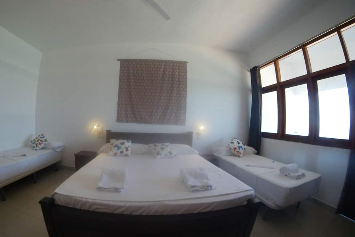 Een hotelkamer met een groot bed, twee kleinere bedden, een wandtapijt en een raam met meerdere ruitjes.
