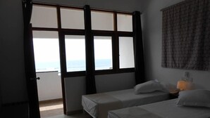 Una habitación con dos camas, un ventanal con vista al mar y una cortina estampada.