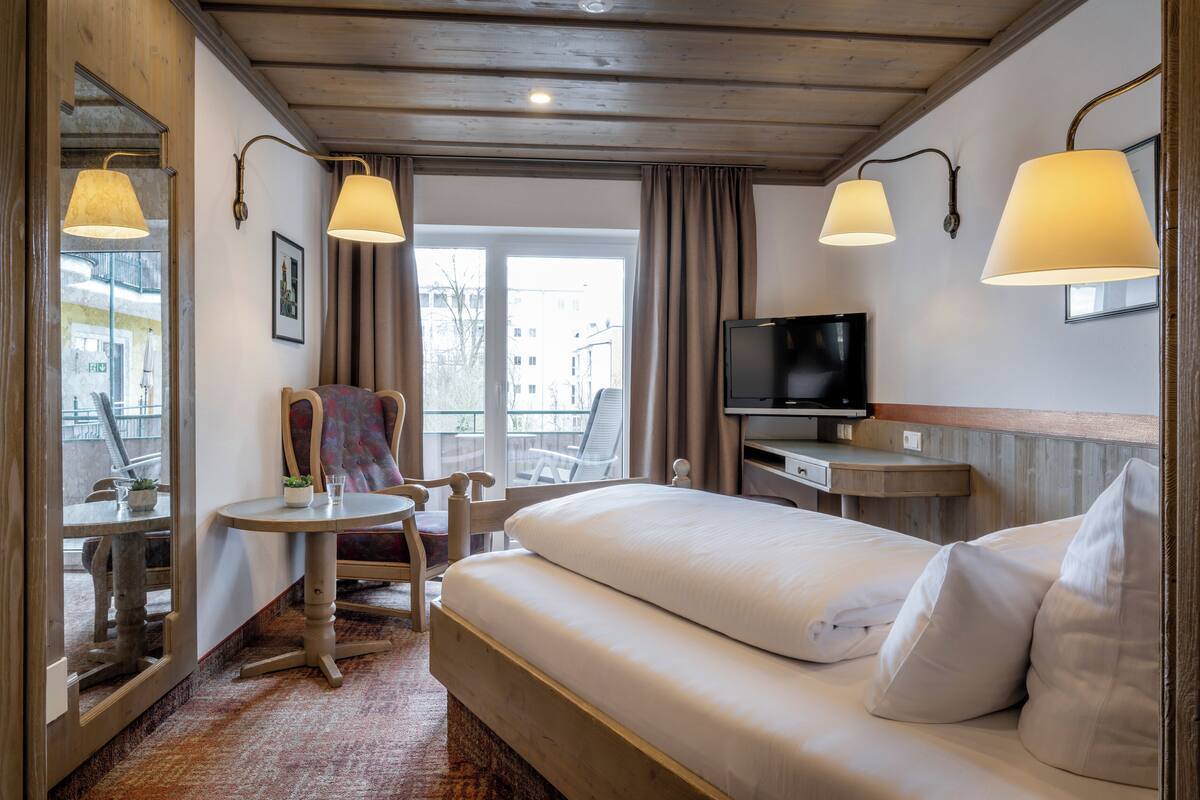 A hotel room with a bed, a TV, a small table with a chair, and a window with curtains.