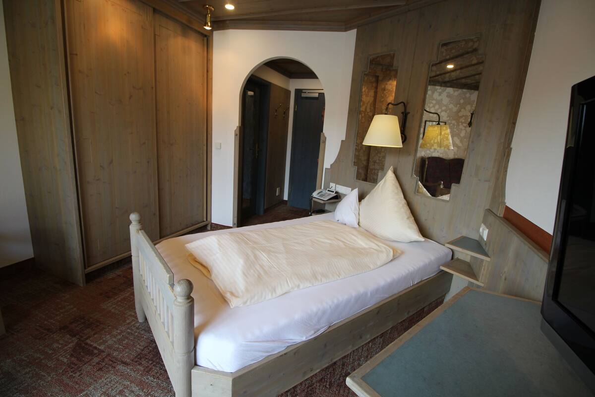 A bedroom with a wooden bed, a nightstand, a lamp, and a television.