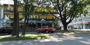 A hotel with a yellow facade, outdoor seating, and a red car parked in front.
