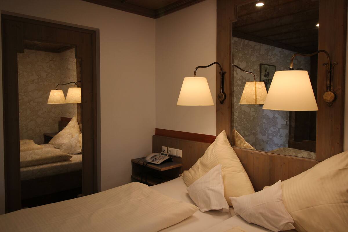 A hotel room with a bed, bedside lamp, nightstand, and a mirror reflecting the room.
