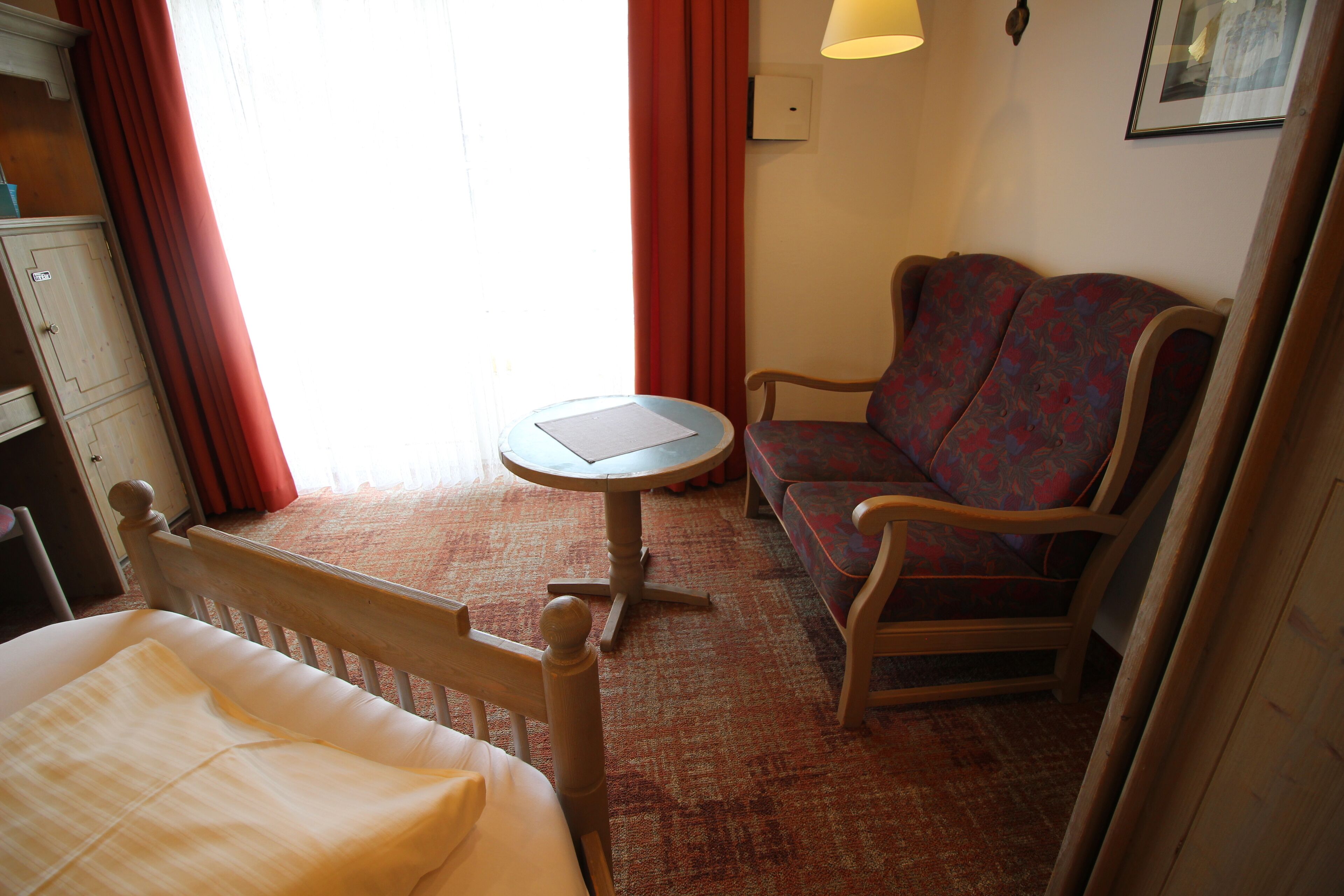 Quarto de hotel com uma cama, uma mesinha redonda, um sofá e um guarda-roupa de madeira.